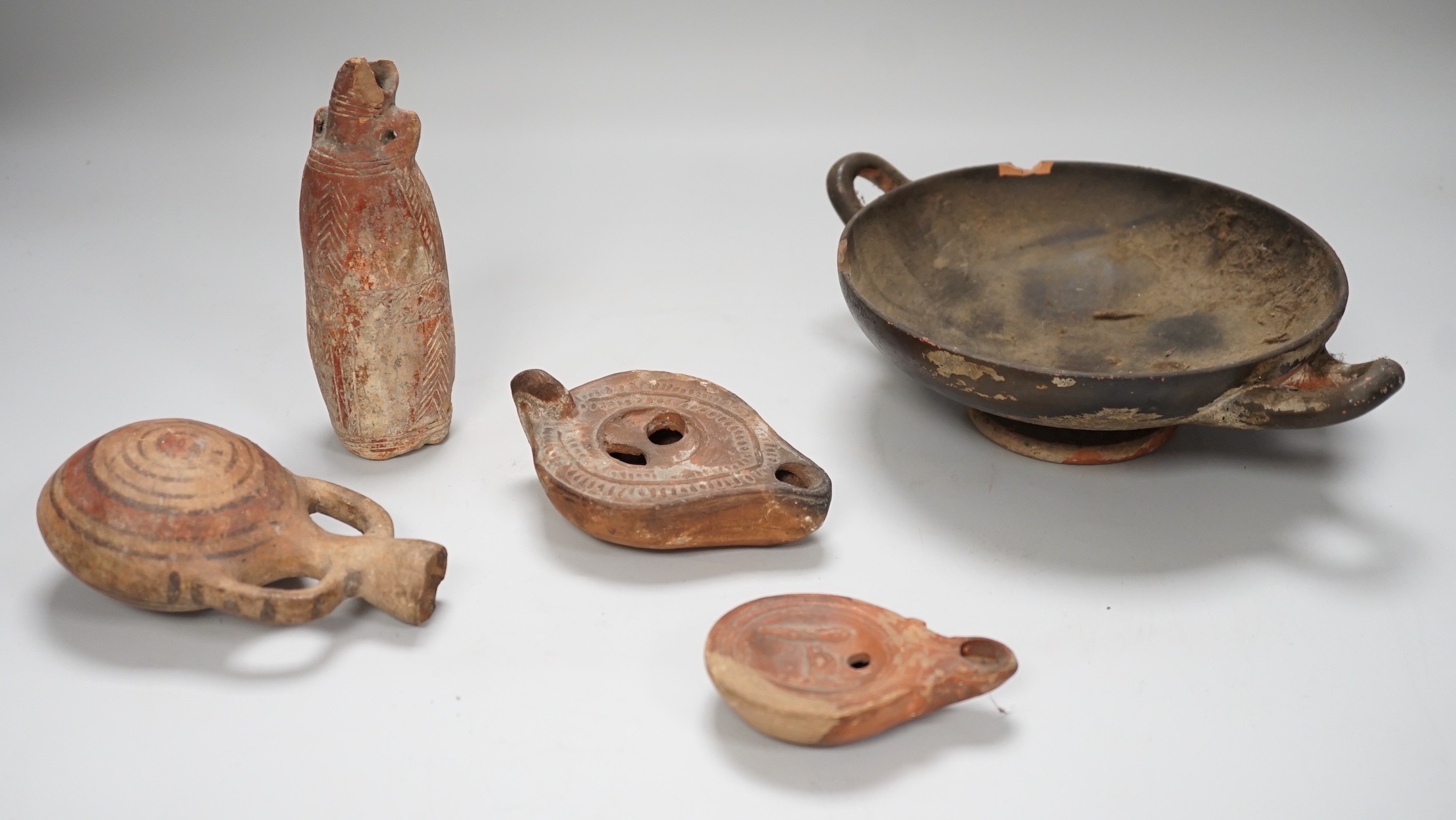 An Apulian black painted kylix, c. 4th century BCE., a Cypriot pottery flask, early Iron Age, two Roman terracotta oil lamps and another archaic vessel, tallest 14cm